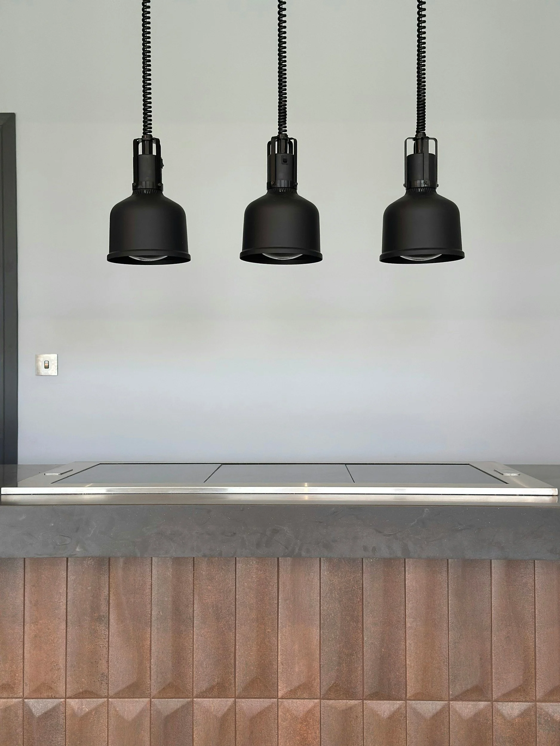 Induction cooktop on a kitchen bench beneath black pendant lights