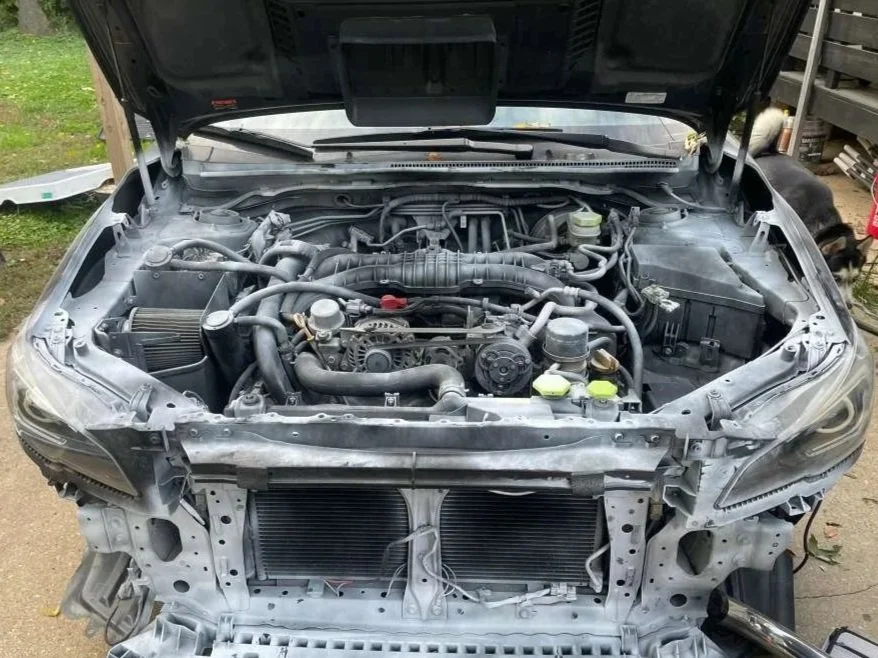Front view of a car with the hood open, showing the engine and various engine components, with the front bumper removed.
