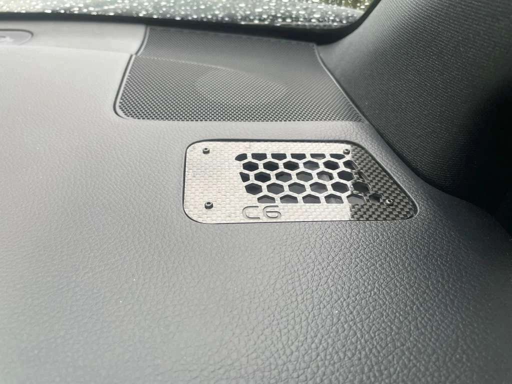 Close-up of a metallic speaker grille with a honeycomb pattern on a car dashboard.
