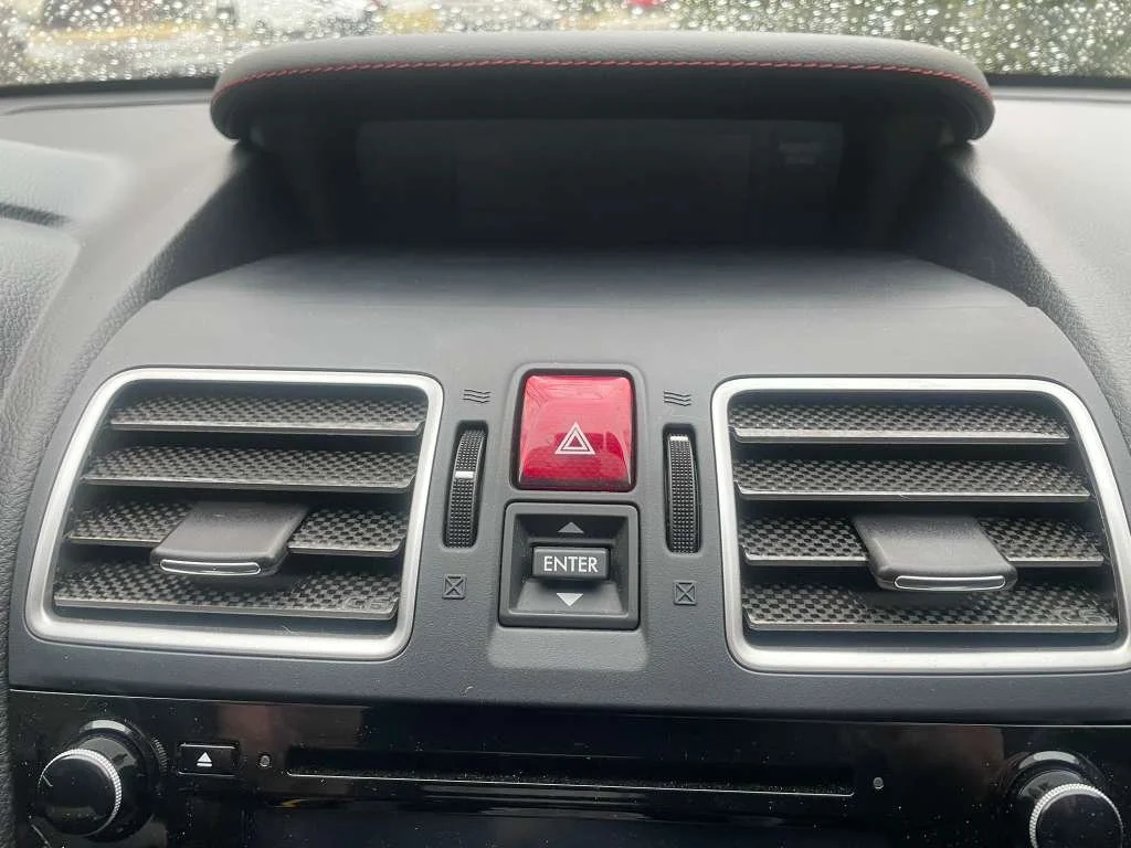 Car dashboard featuring two rectangular air vents, a red hazard light button, an 'Enter' button with arrow buttons, and a black control knob.