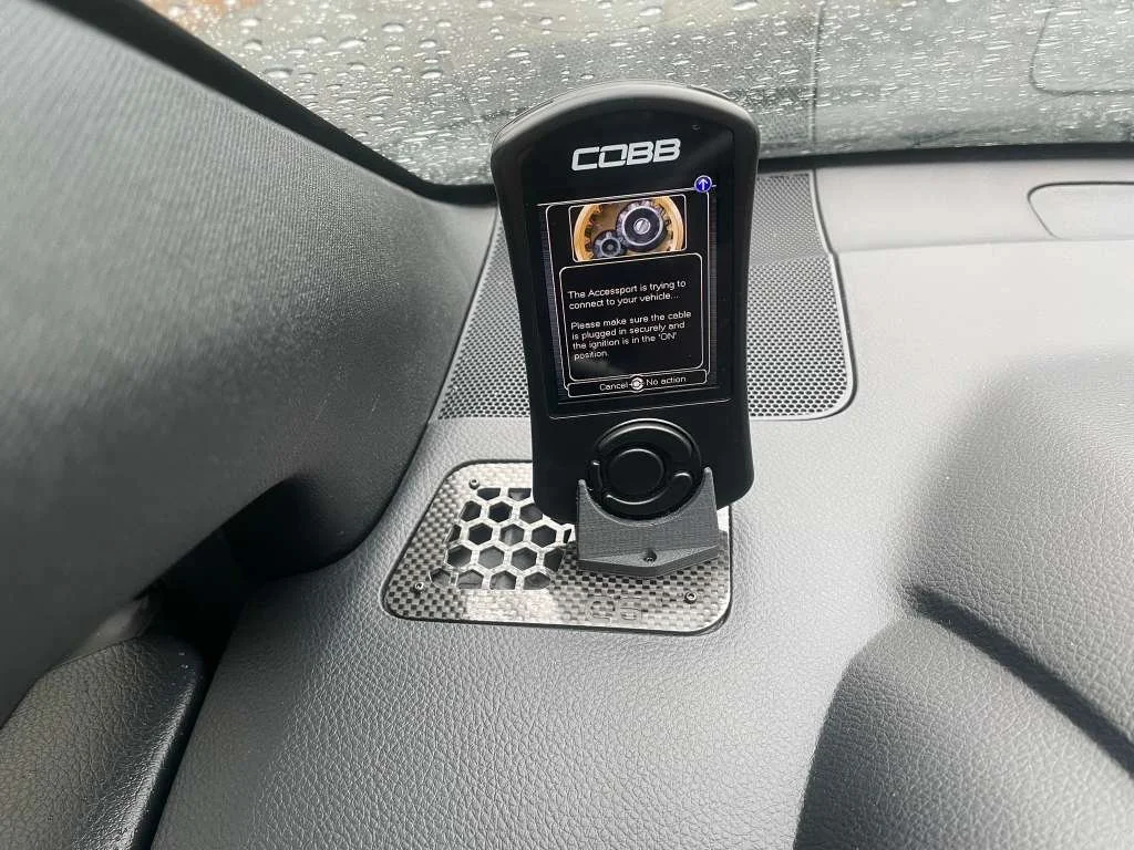 A Cobb Accessport device mounted on a vehicle's dashboard with a message on the screen indicating it is attempting to connect to the vehicle.