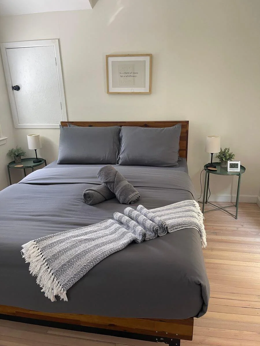 Clean Airbnb bedroom with neatly made bed, folded towels, bedside lamps, and guest-ready staging