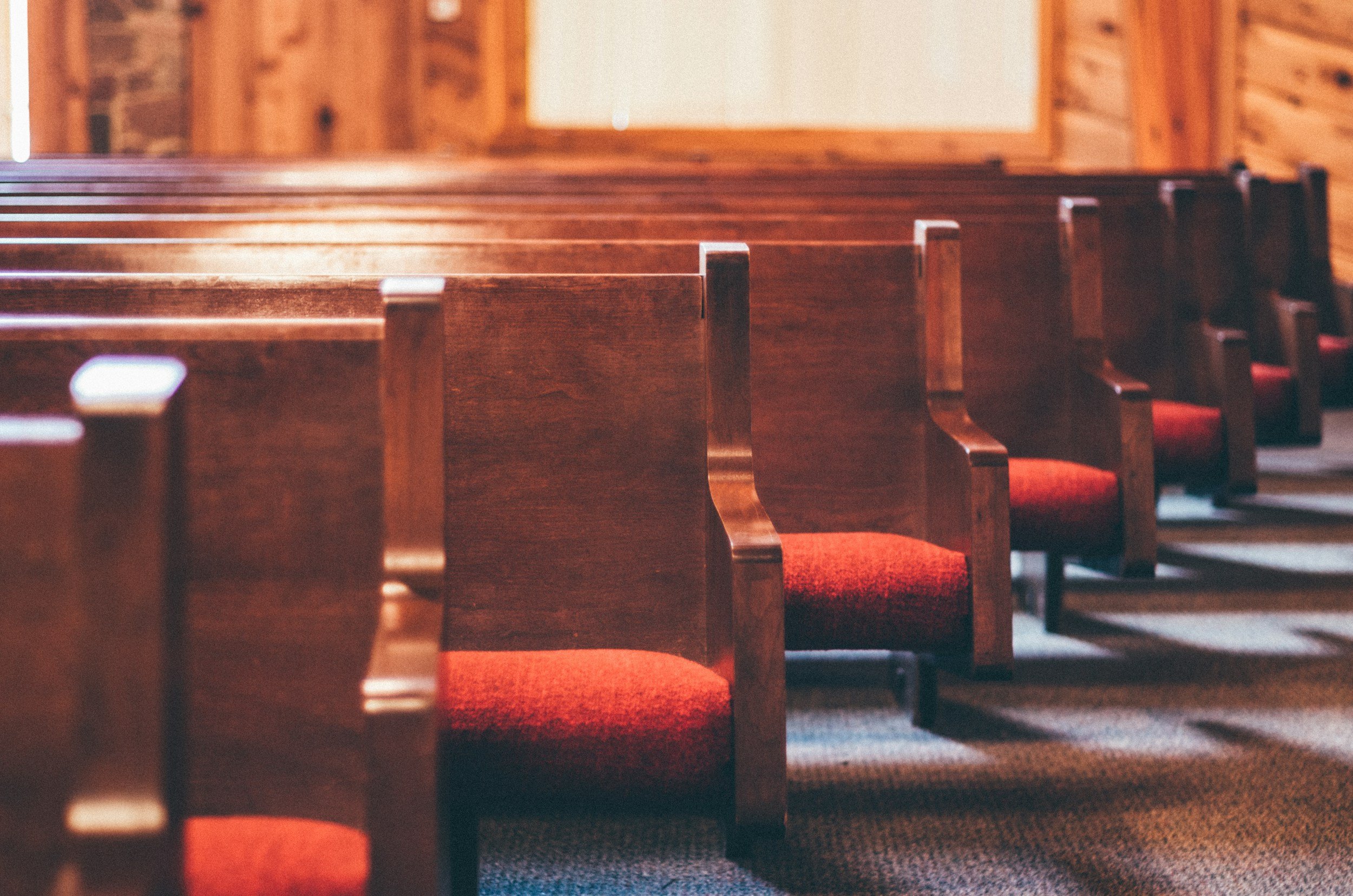 Wooden church pews inside a worship hall with red seating and aisle.