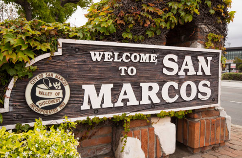 Wooden city sign reading 'Welcome to San Marcos' with greenery and brick supports