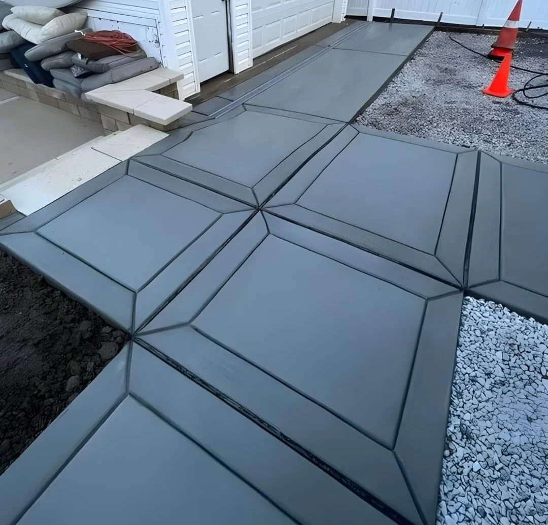 Recently installed concrete patio with geometric pattern next to a house, with construction cones and tools nearby.