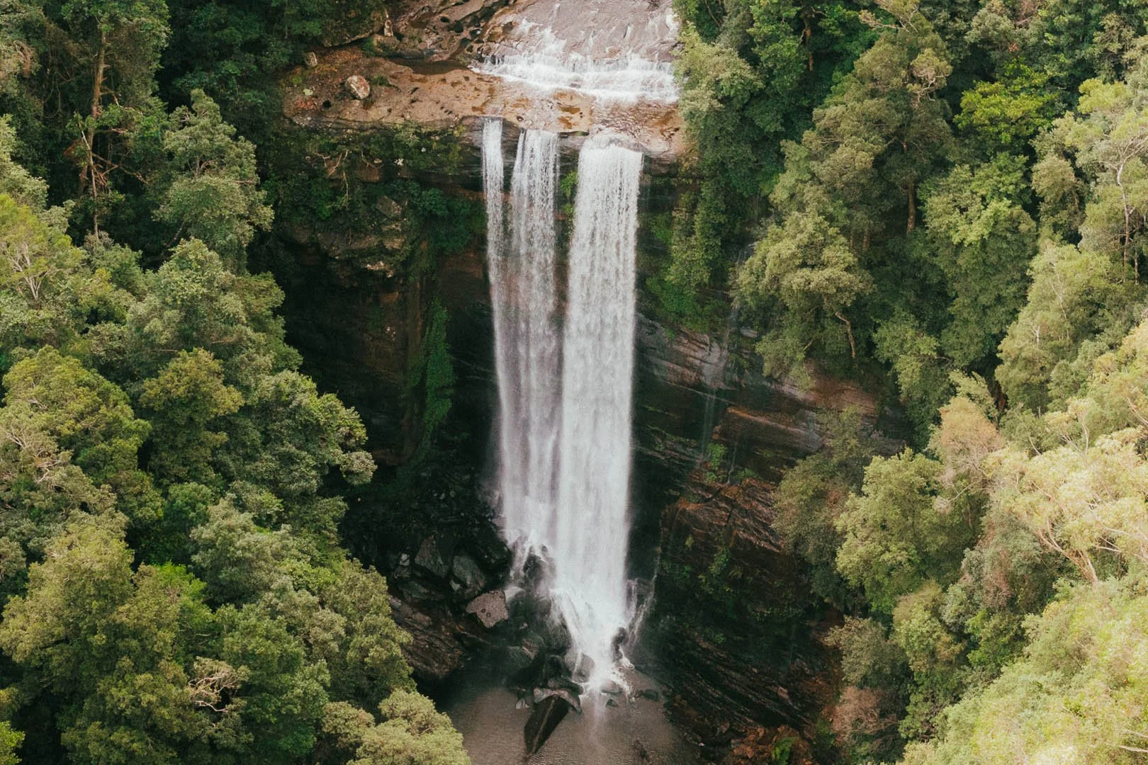 Aerial view of a waterfall cascading down a rocky cliff surrounded by dense green forest.