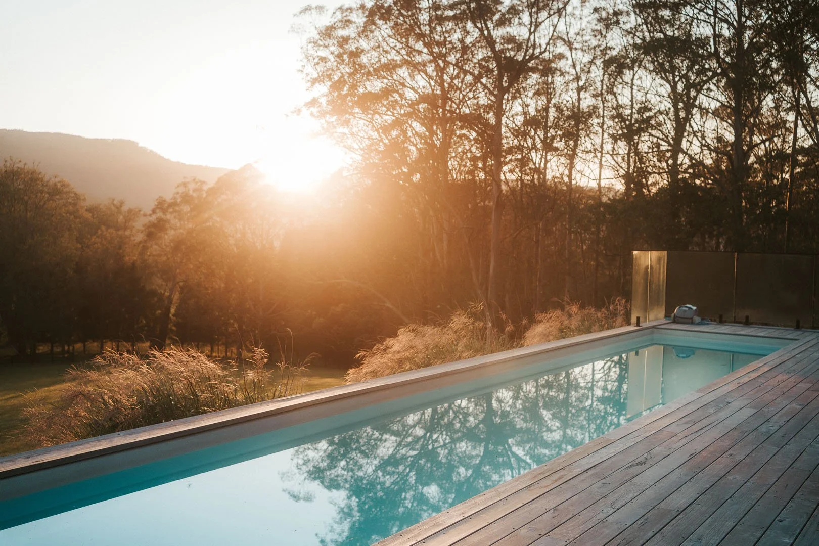 Sunset over a mountain landscape with a backyard pool and wooden deck.