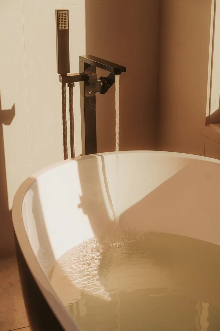 Bathtub with water running from a modern black faucet in a bathroom with beige tiles and wall.