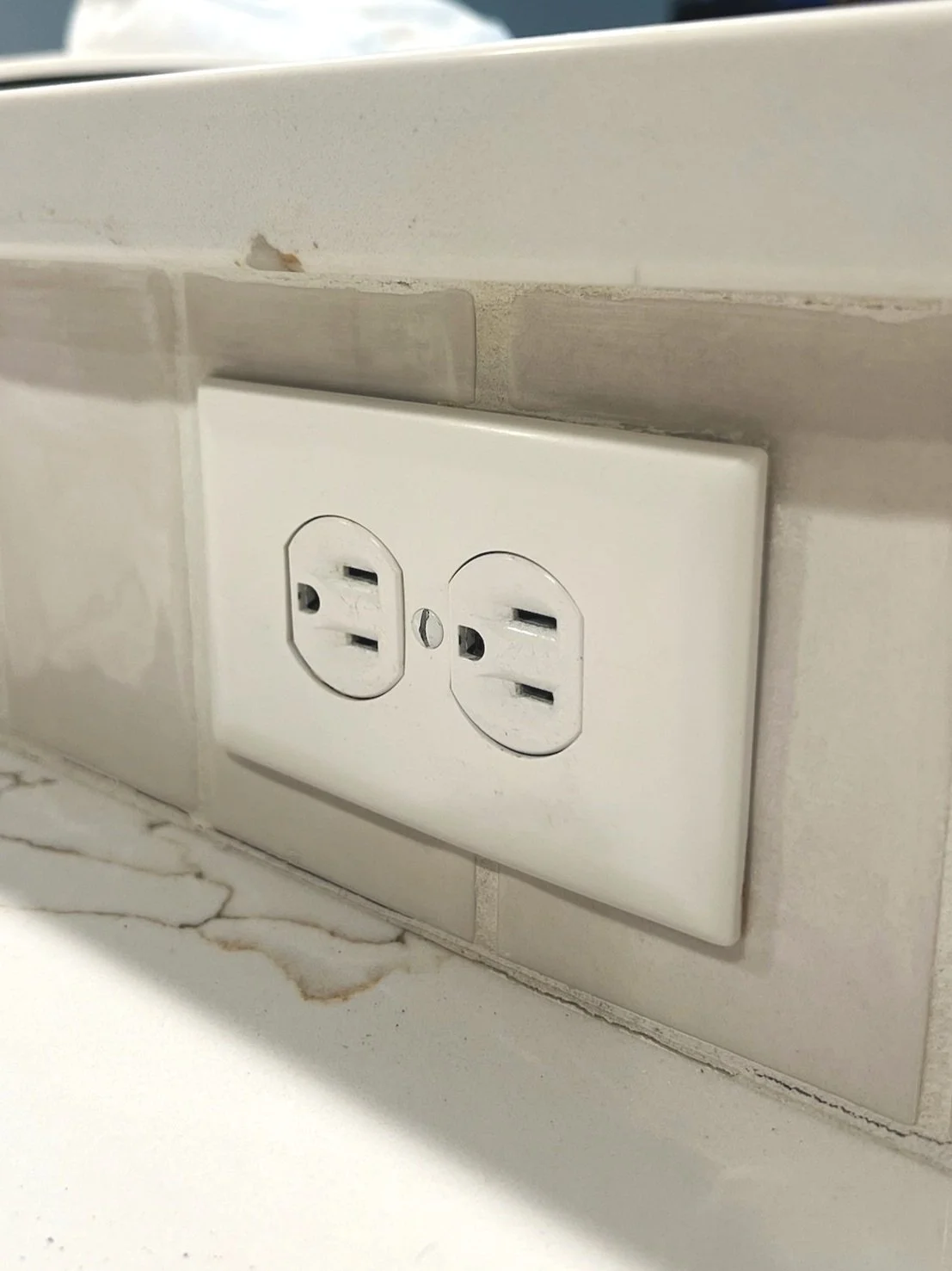 New white GFCI electrical outlet installed above marble kitchen countertop by Walter Electrical Contractors for safe residential wiring.