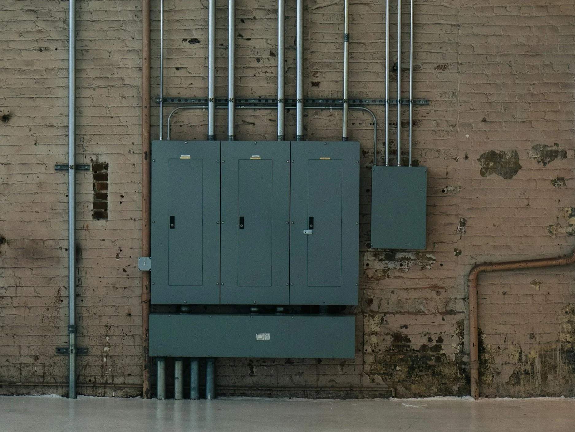 Electrical panel and conduit on a brick wall, showing that Walter Electrical Contractors installs and does maintenance on panels and breaks. Walter Electric also does whole home surge installs.