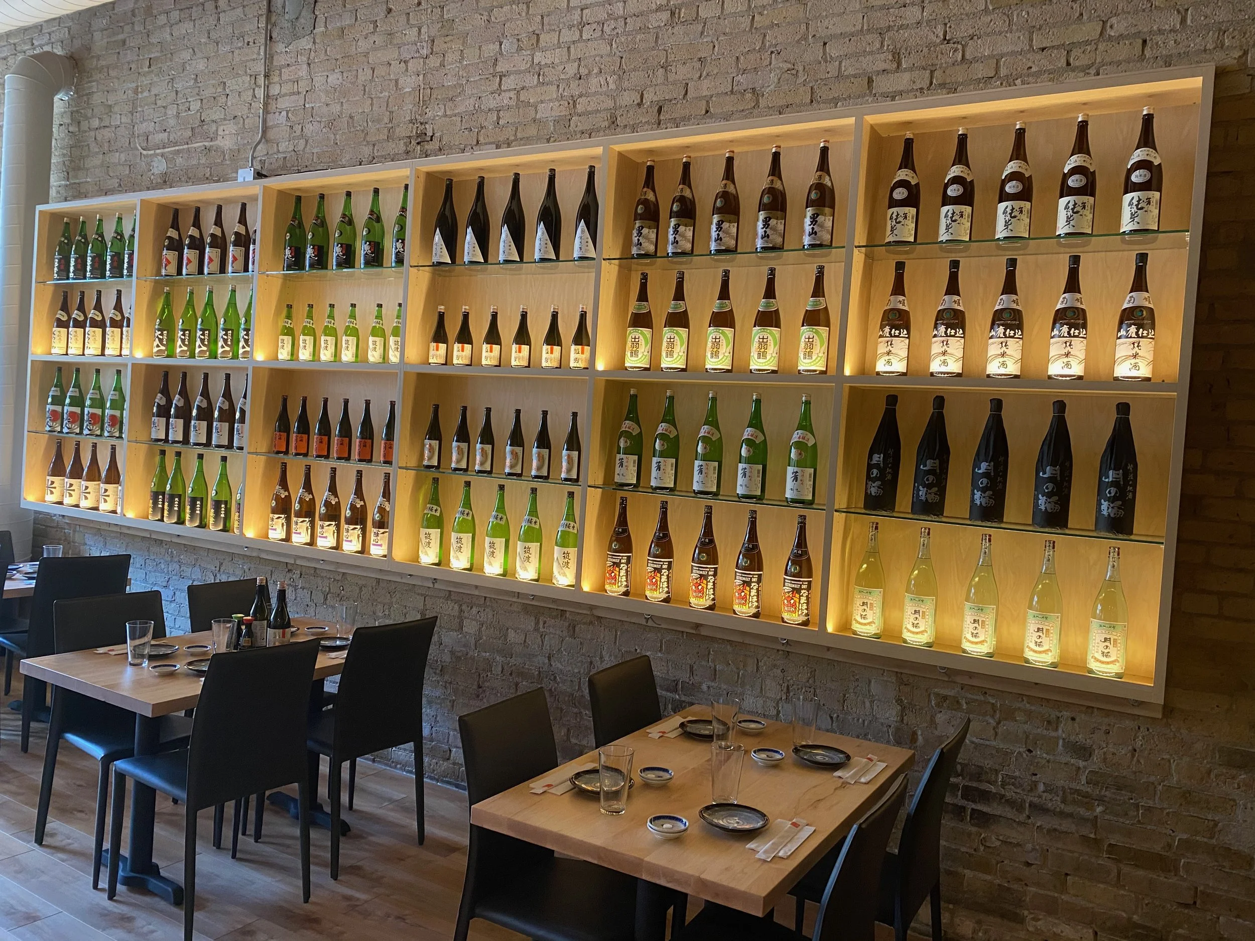 Custom backlit shelving and ambient dining area lighting installed by Walter Electrical Contractors in Minnesota, highlighting illuminated sake bottles and table lighting in a brick-walled restaurant.