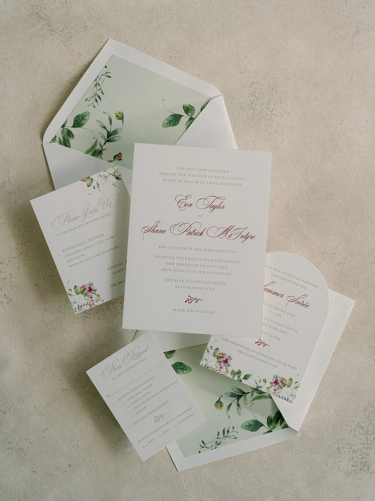 Wedding invitation set including multiple cards with floral and greenery designs, placed on a beige surface.