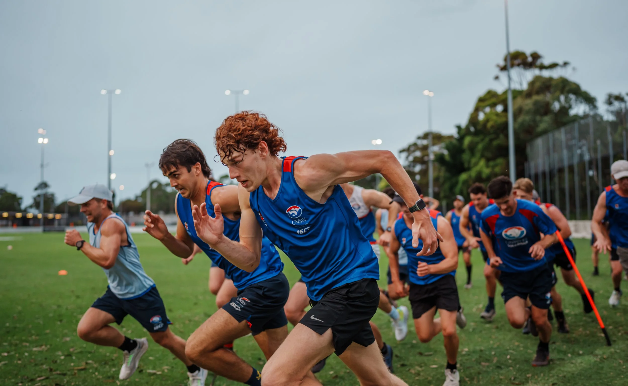 A group of cross country runners in blue athletic gear starting a race on a grassy field.
