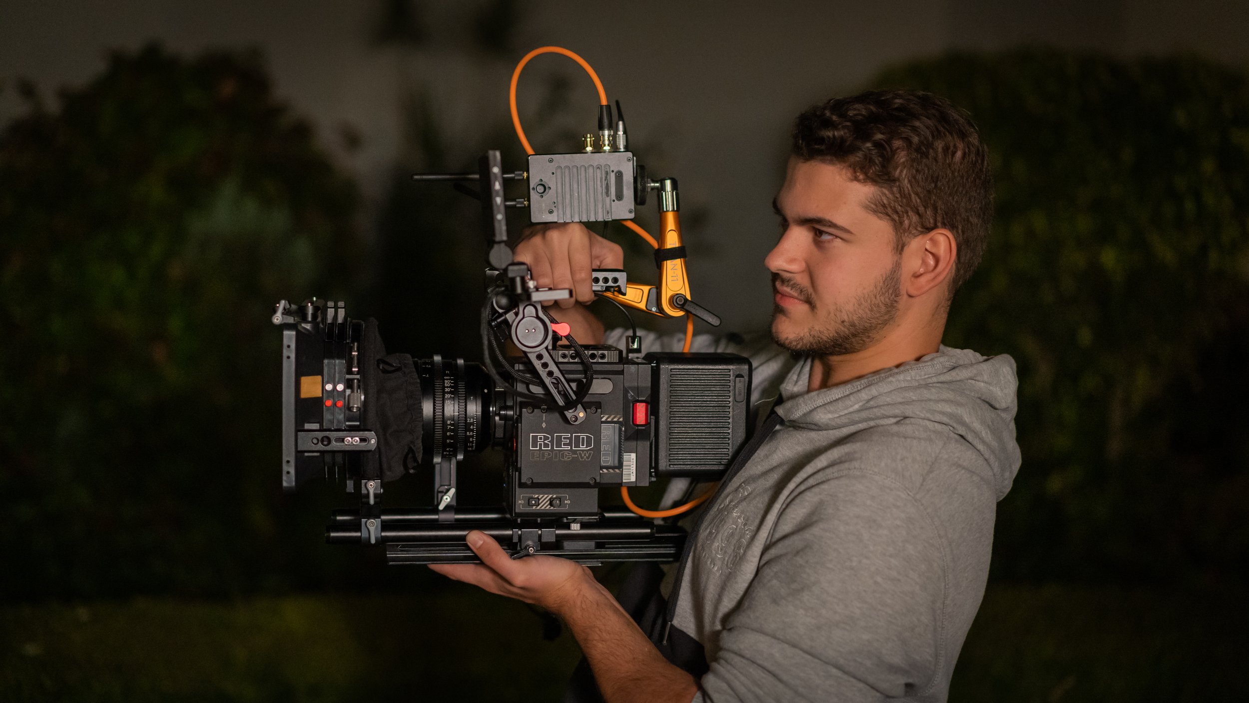 A man operating a professional cinema camera outdoors at night.