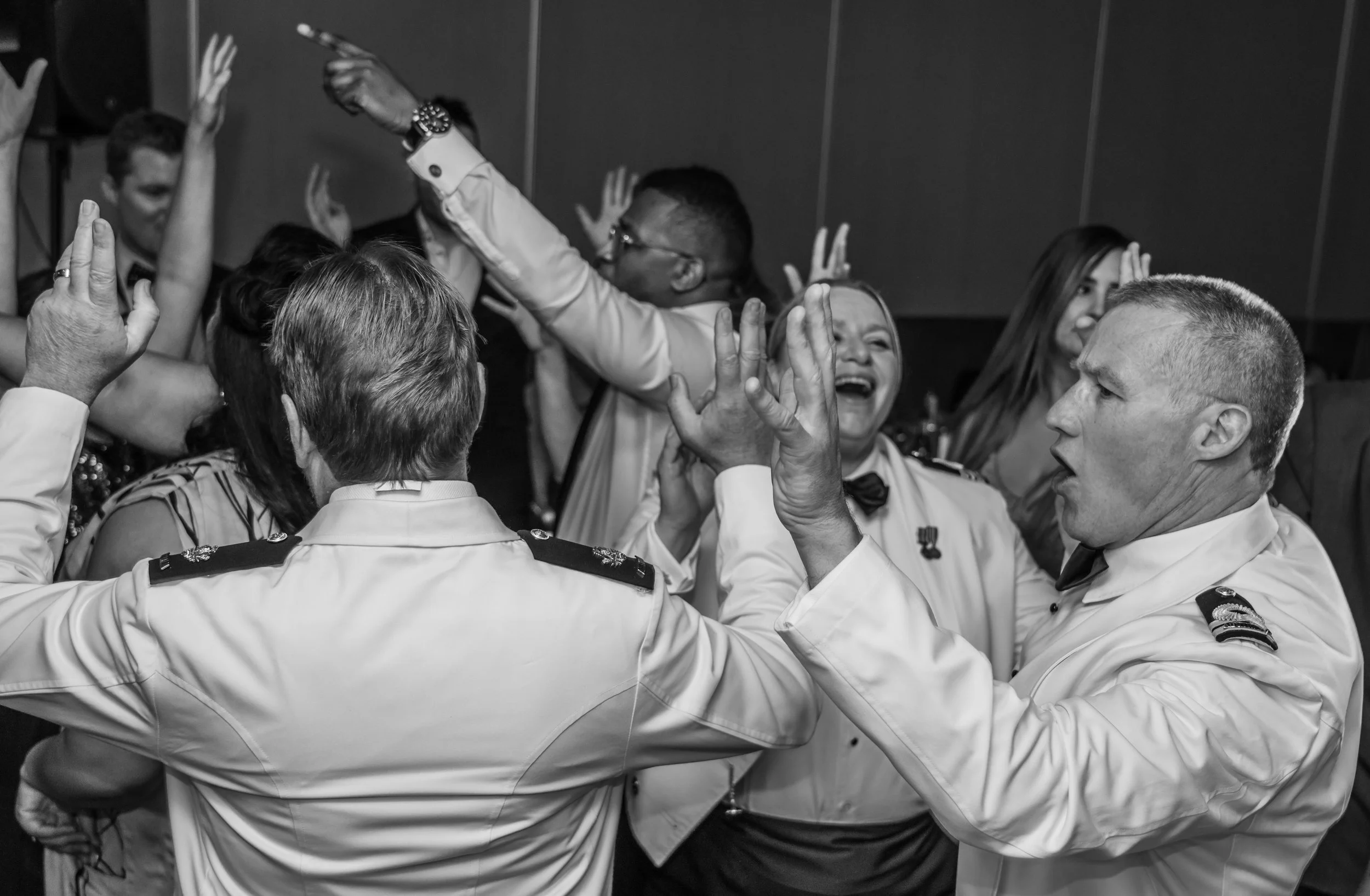 Black and white photo of uniformed military officers and civilians celebrating and dancing together at an event.
