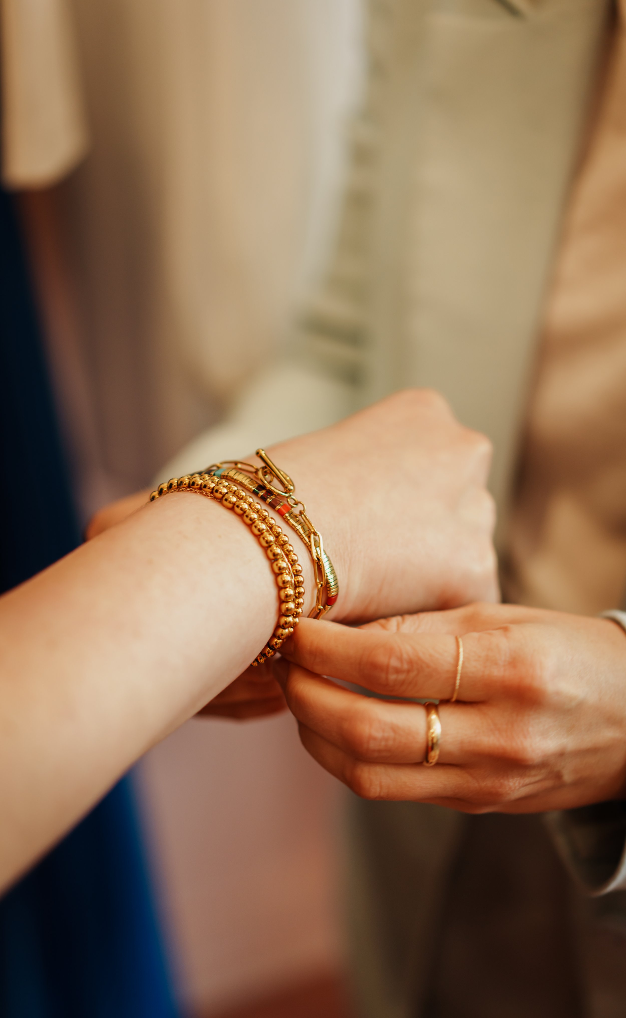 Close-up of two hands holding each other, one person wearing multiple gold bracelets and a thin gold ring on their finger.