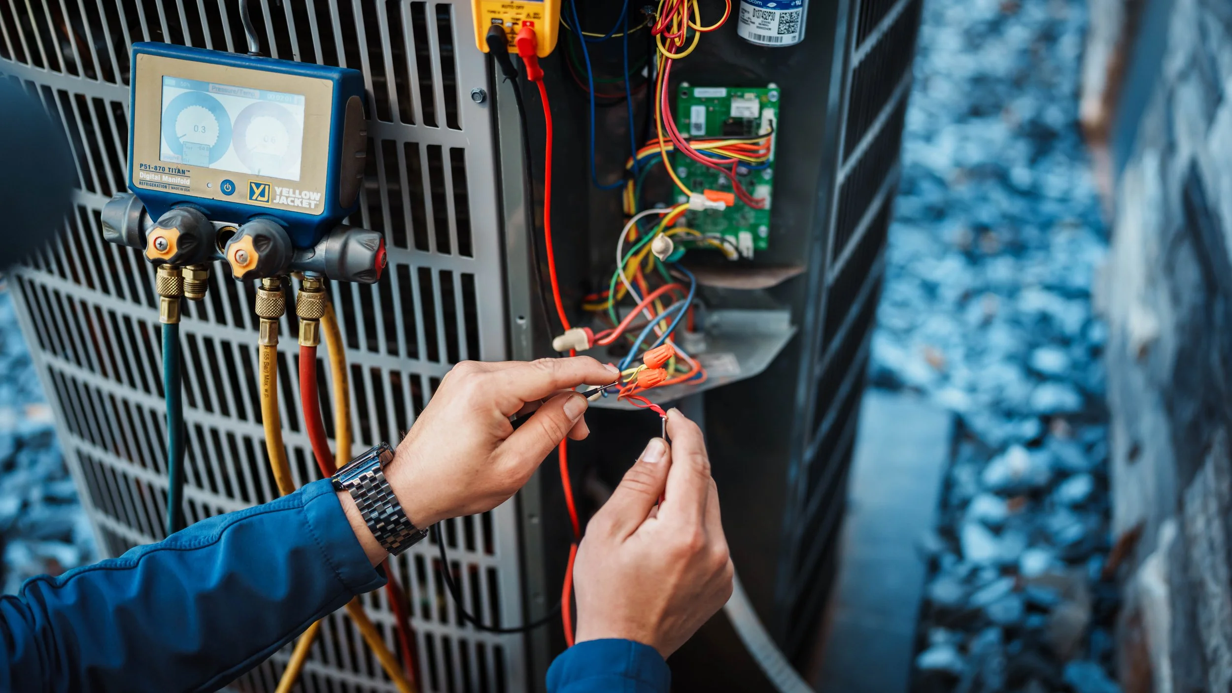 Technician repairing or maintaining an HVAC unit, focusing on a circuit board and wiring inside the outdoor unit.