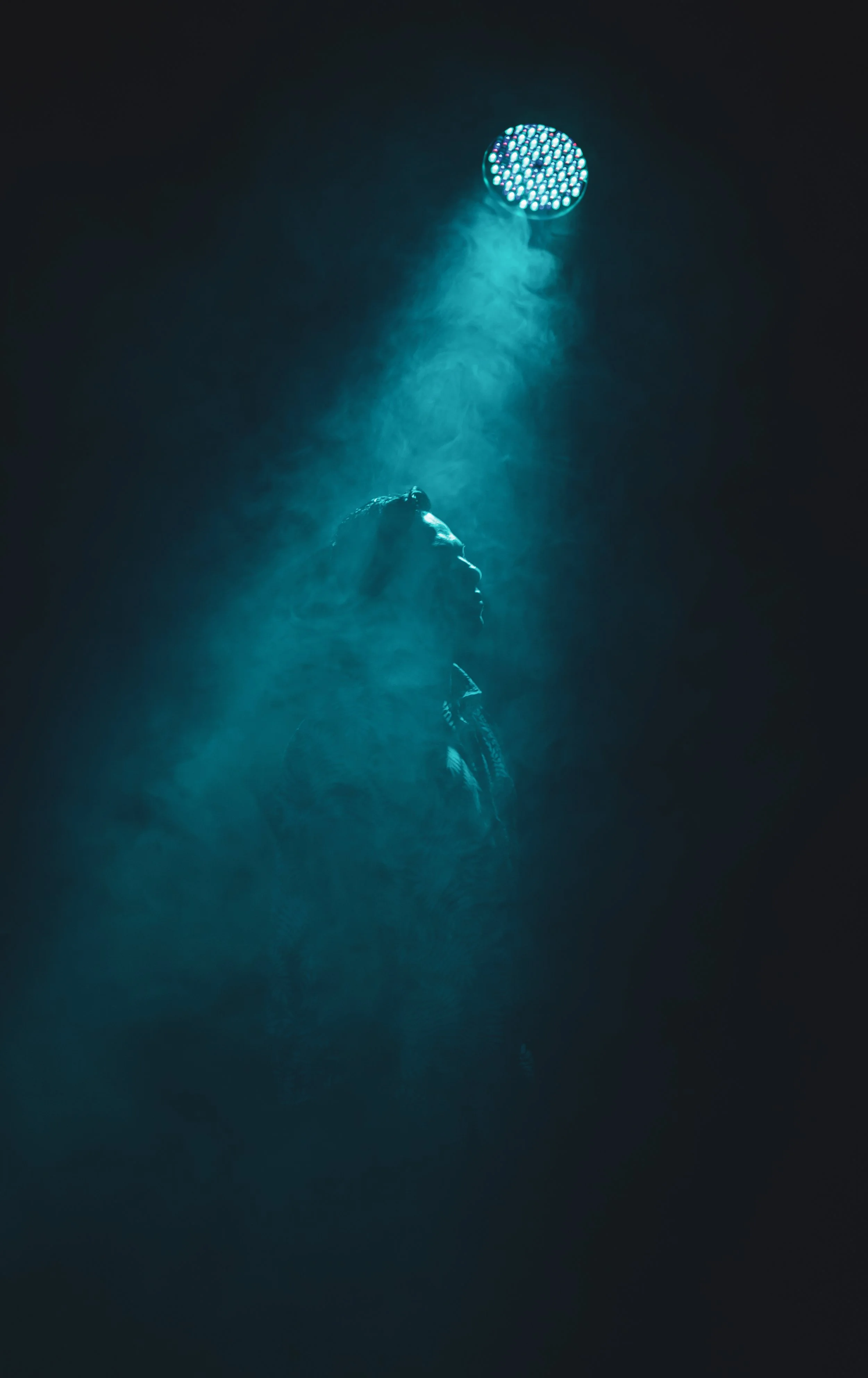 A person in profile, illuminated by a blue spotlight in a dark, foggy setting.