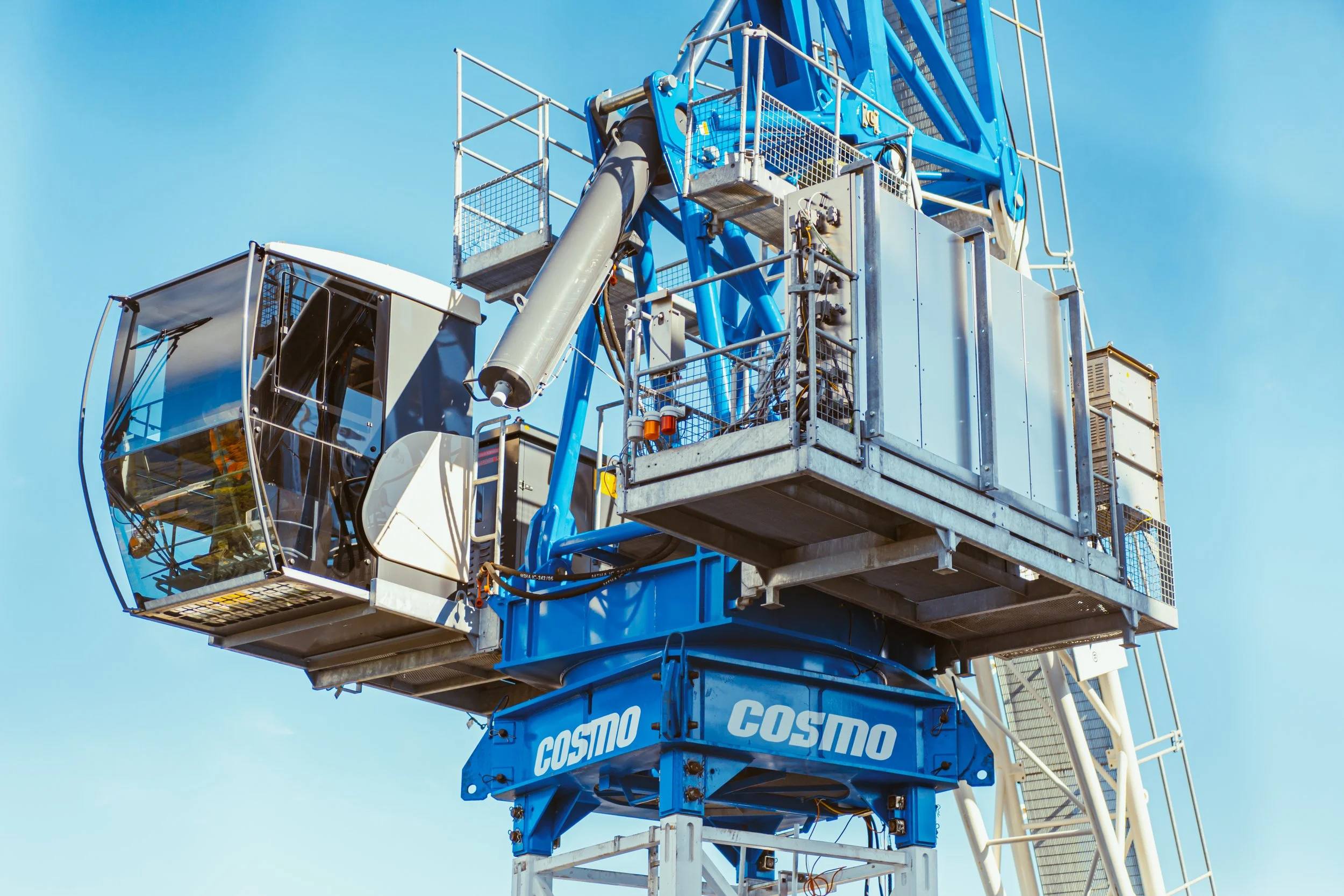 Close-up of a large blue construction crane with a glass-enclosed operator cabin, against a clear blue sky.