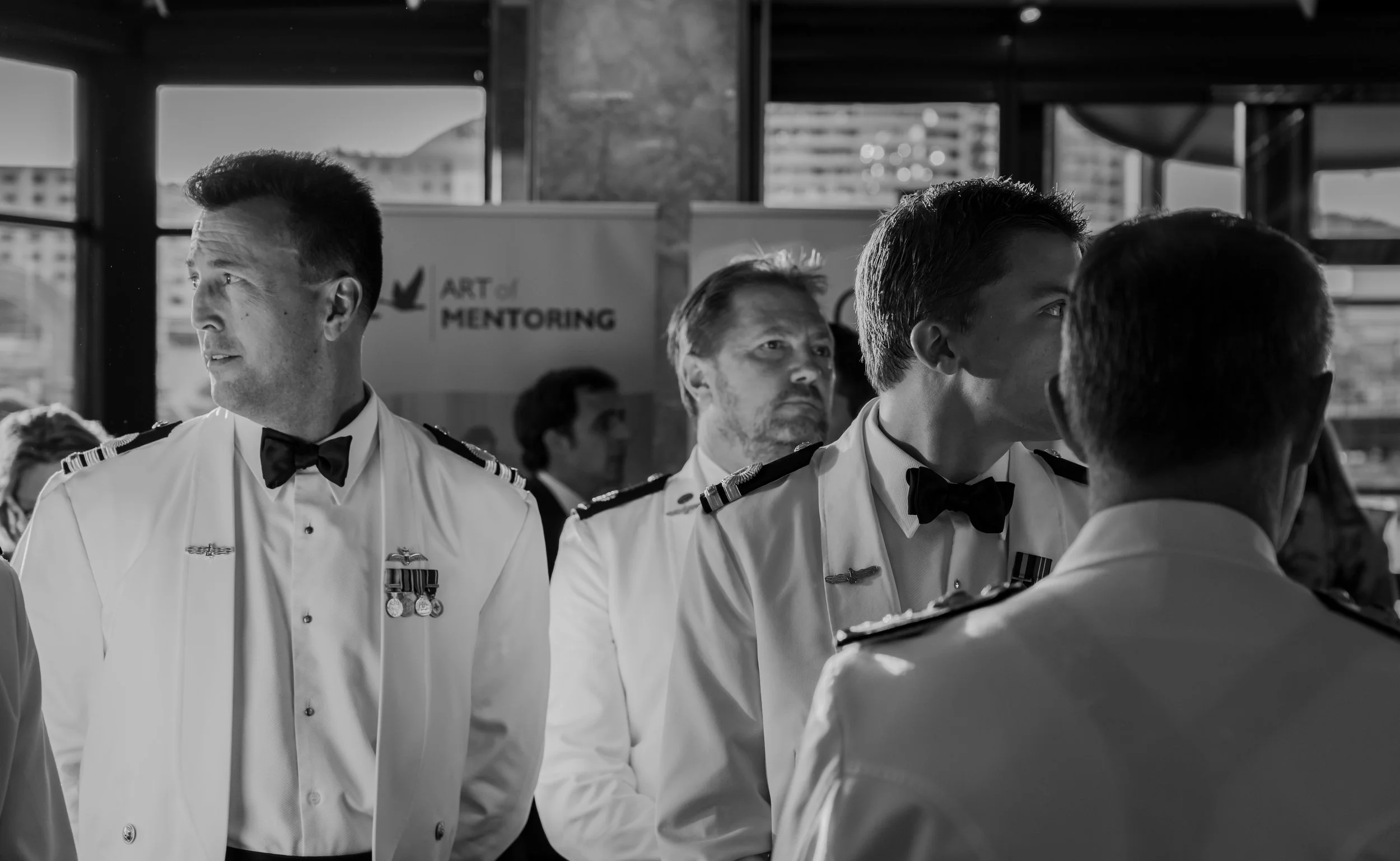 Men in military dress uniforms attending a formal event, with a banner in the background that reads 'Art of Mentoring'.