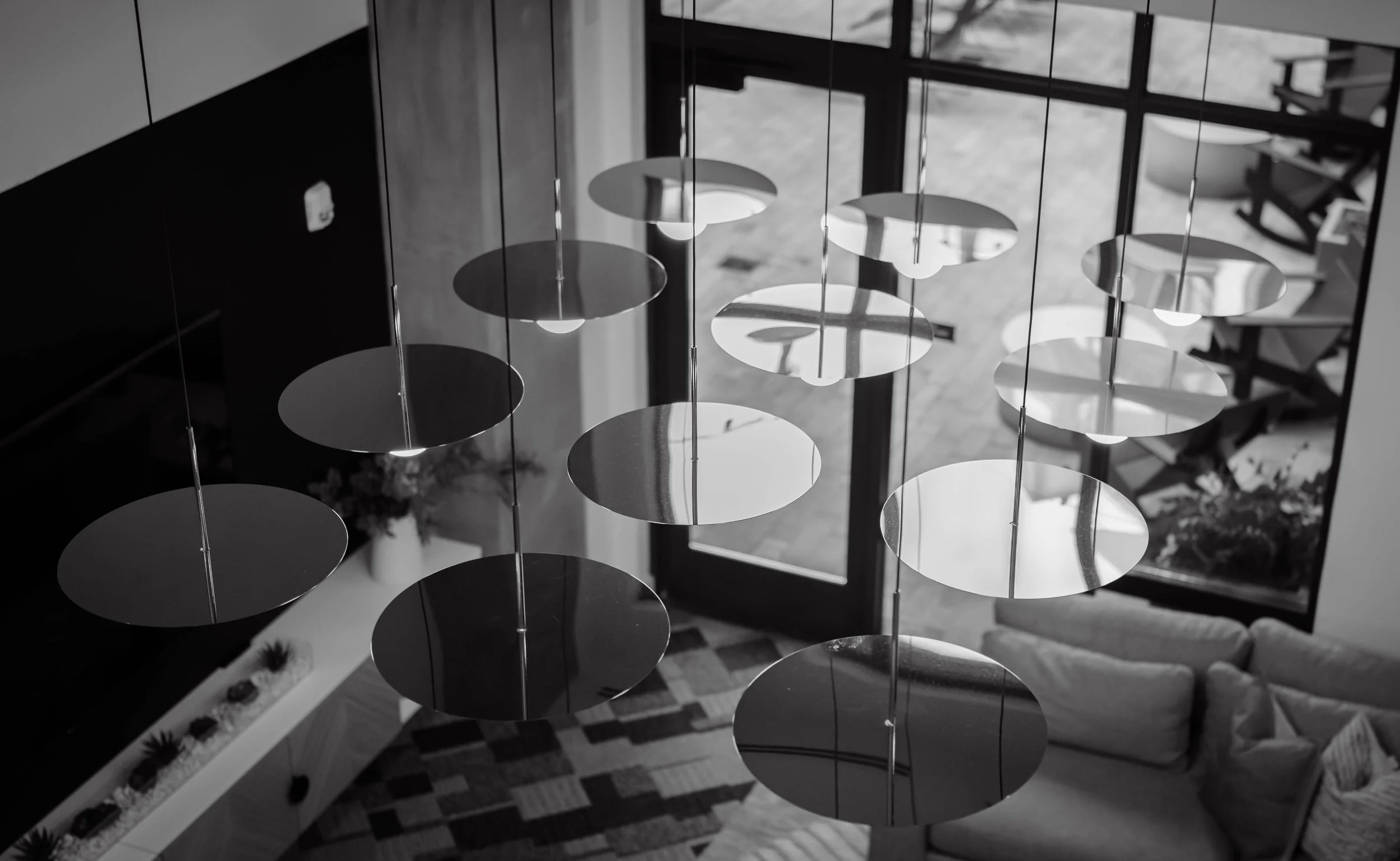 Black and white aerial view of a modern living room with hanging circular pendant lights, a sofa, and a glass door leading outside.