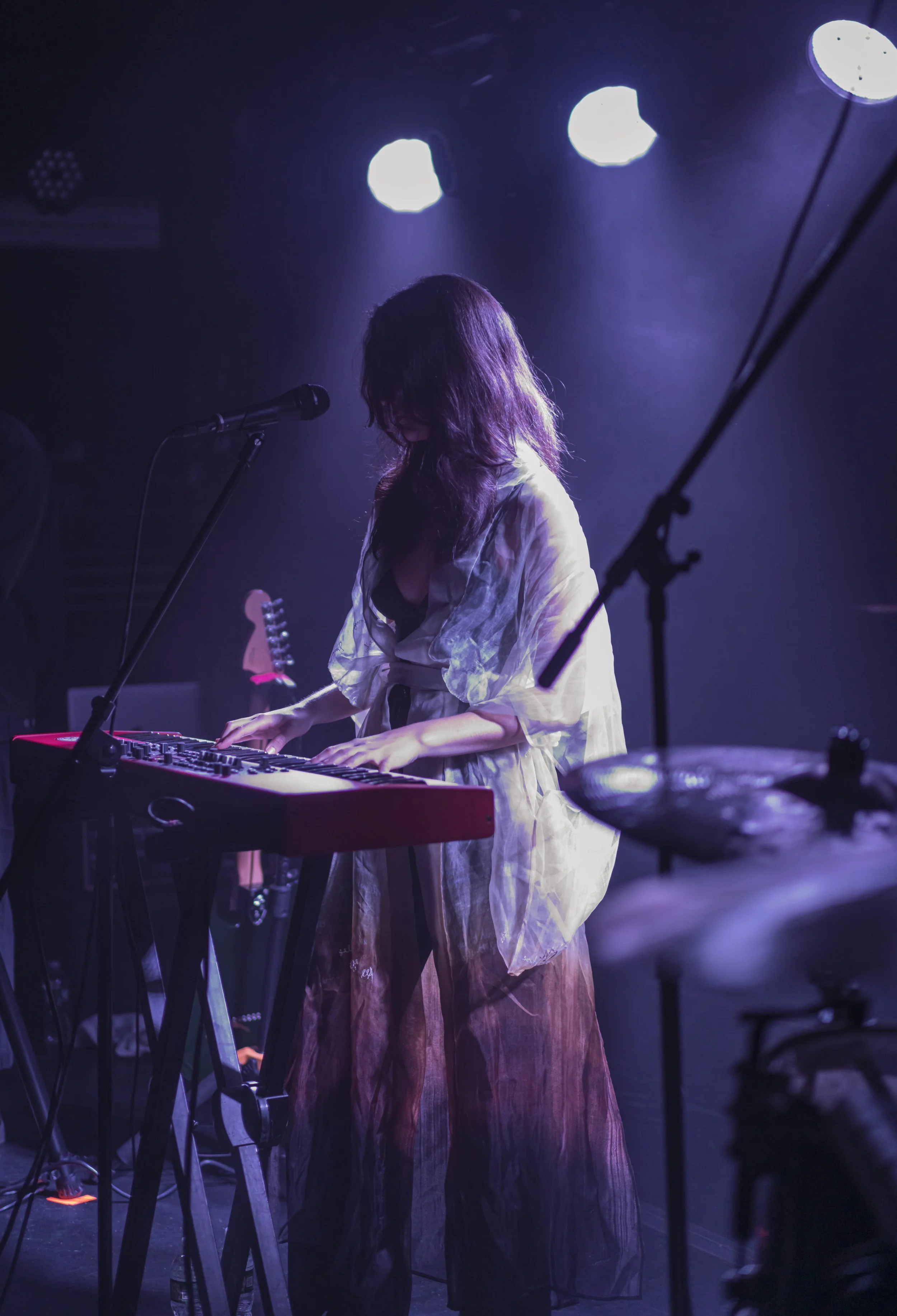 A woman playing a keyboard on stage during a live performance with purple stage lighting.