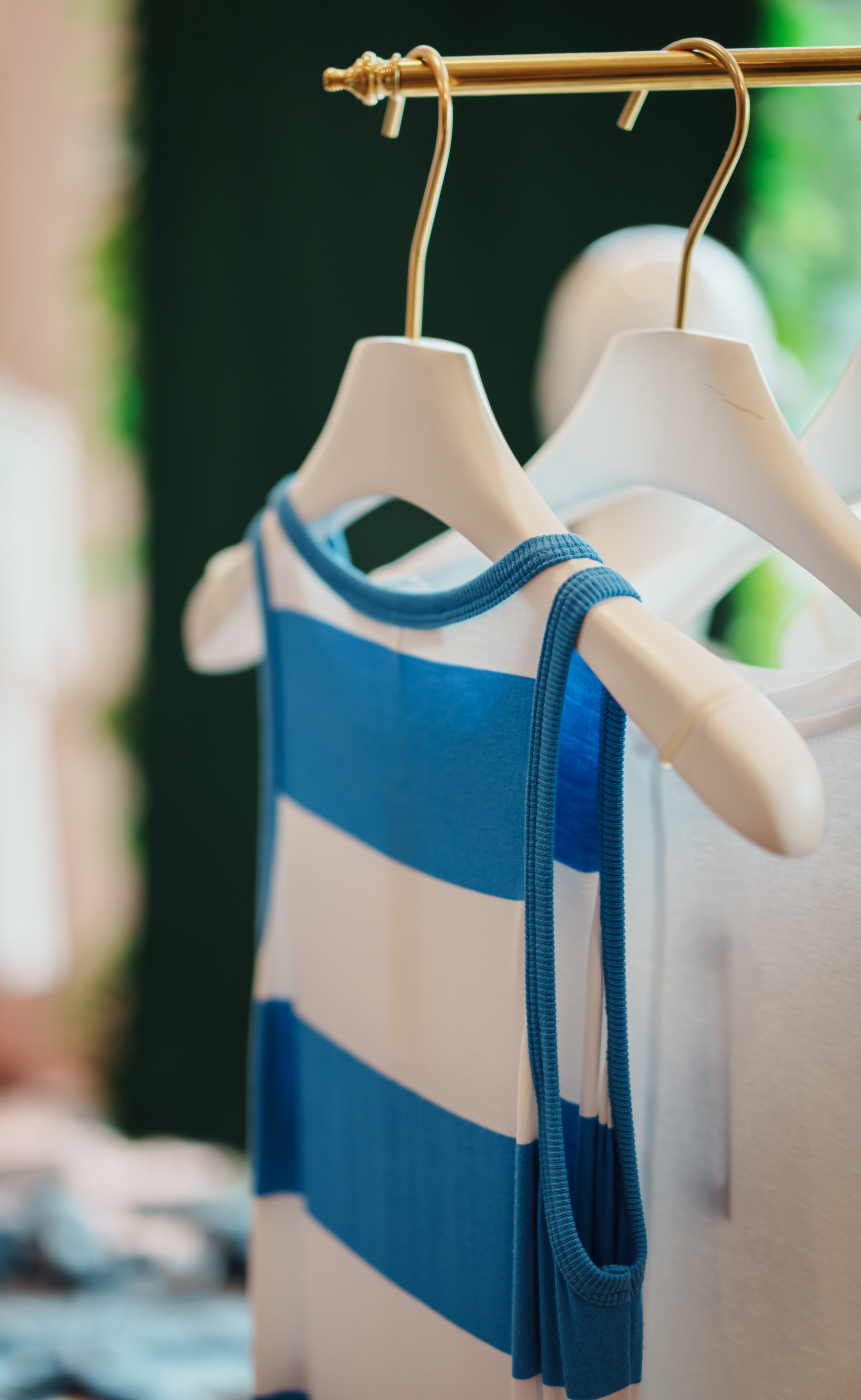 Blue and white striped sleeveless dress hanging on a white hanger on a clothing rack.