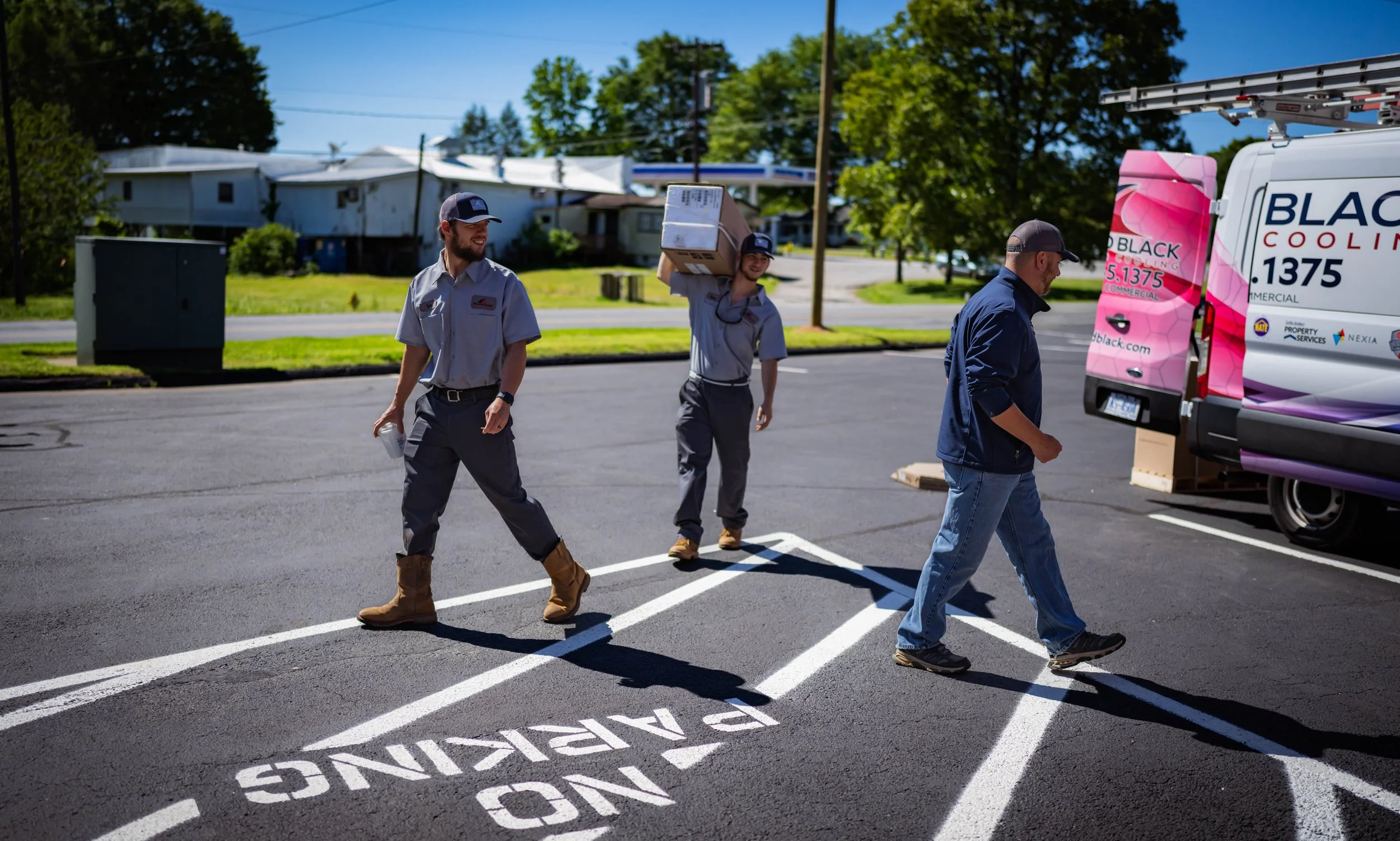 Construction workers walking on a newly paved parking lot with a recycling zone marked on the ground, and a colorful truck in the background.