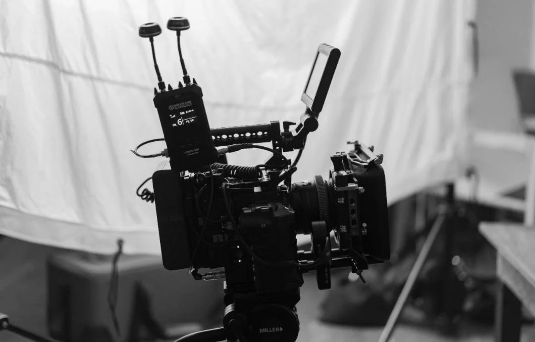 Black professional video camera on tripod with various accessories, set up in a studio or production environment.