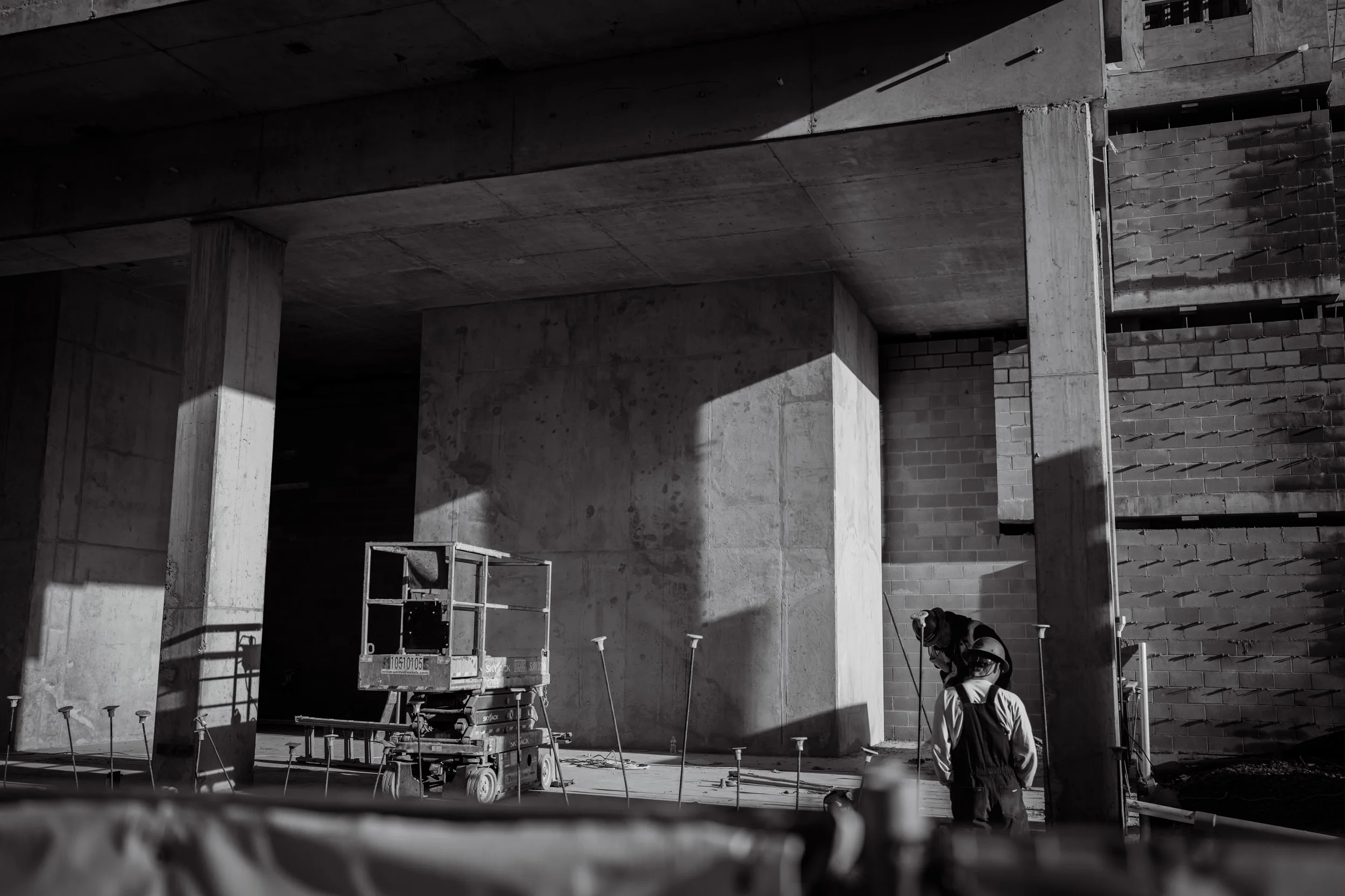 Construction workers inspecting concrete pillar at building site, black and white photo.