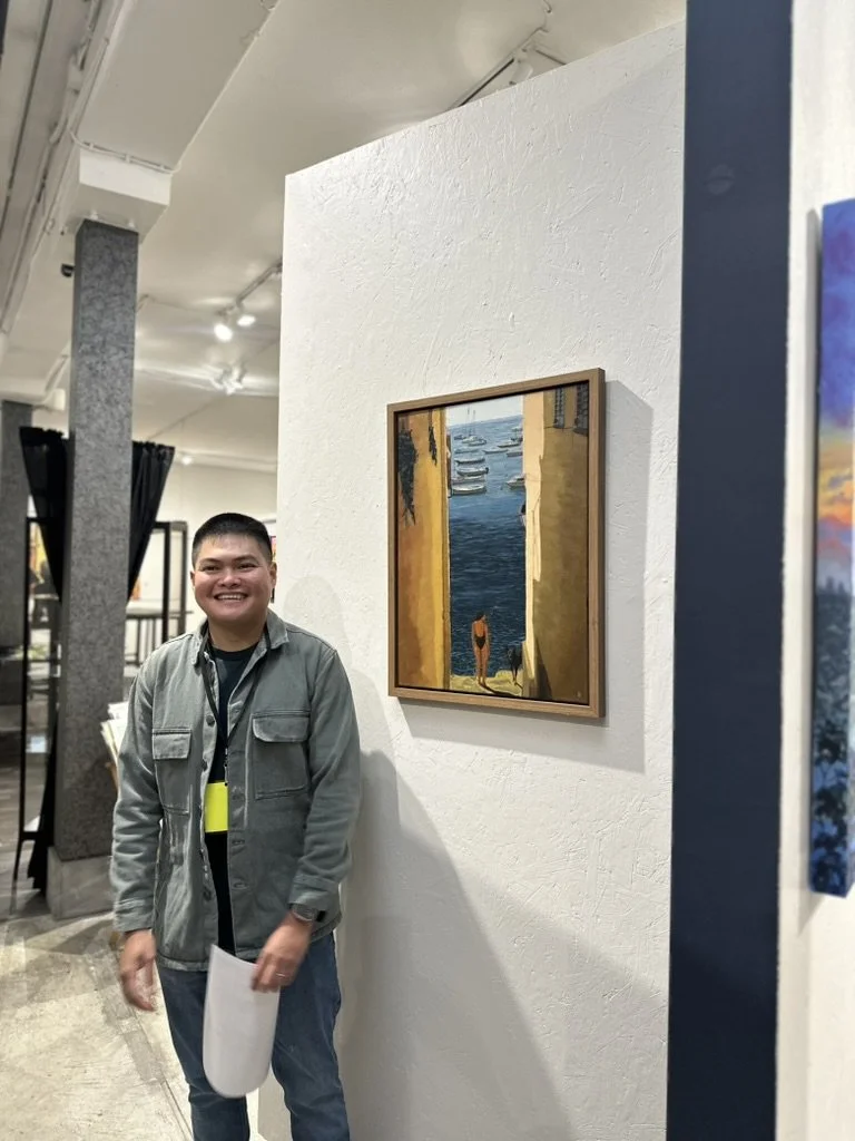 Smiling man standing next to a framed painting of a person looking out at a marina with boats.
