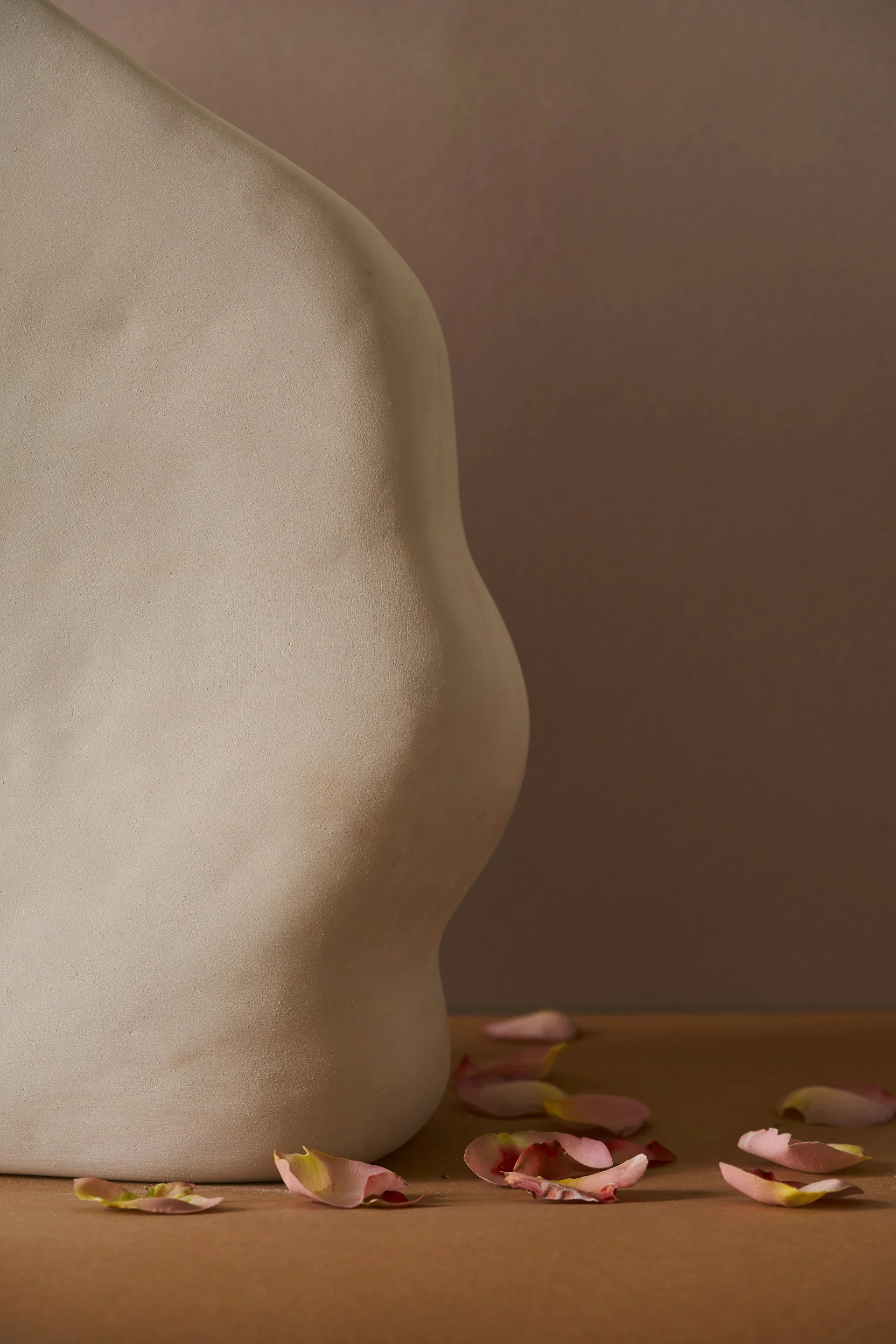 Close-up of a ceramic vase with pink rose petals scattered on the surface near its base.