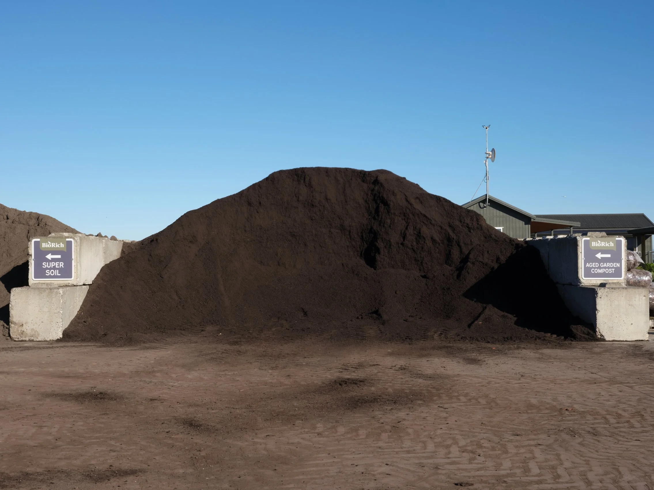 Pile of aged garden compost next to a pile of super soil at a composting facility, with signs indicating each type of compost.