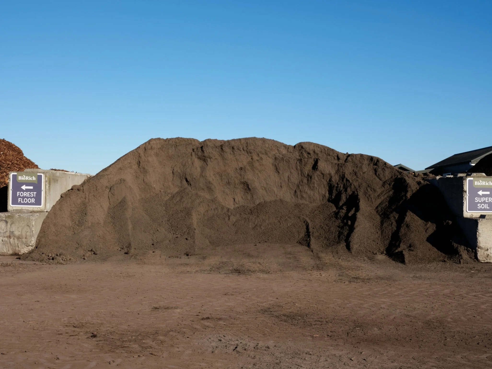 Large pile of soil or compost on a construction or landscaping site with signs indicating different soil zones, under a clear blue sky.