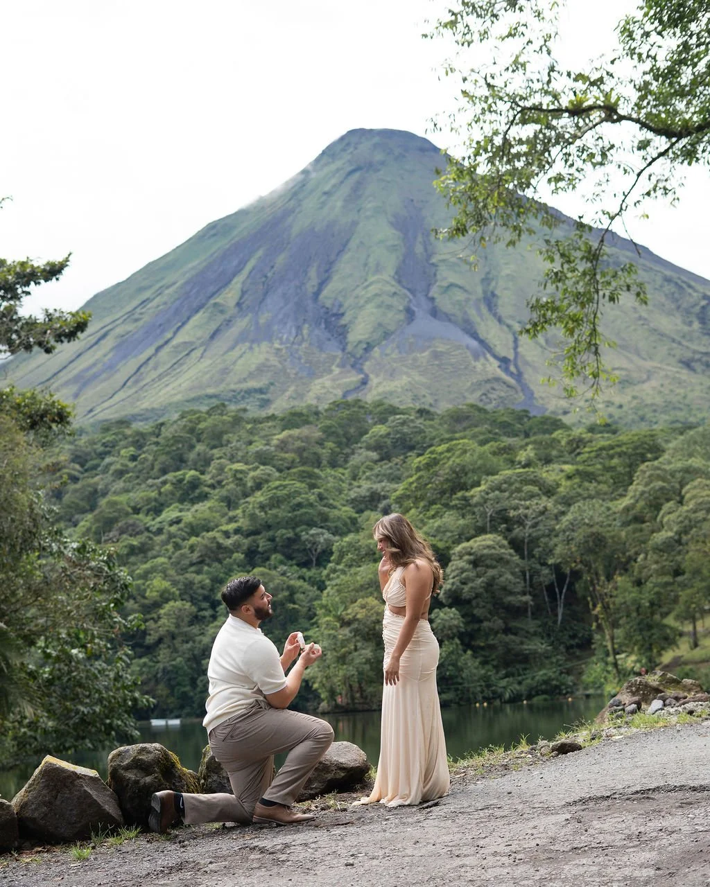 A man proposing marriage to a woman in a natural outdoor setting with a large volcano in the background.