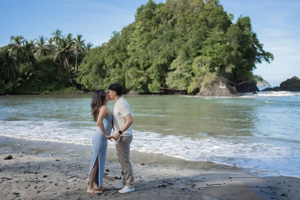 A couple kissing on a beach with a green, tree-covered island of Costa Rica in the background.
