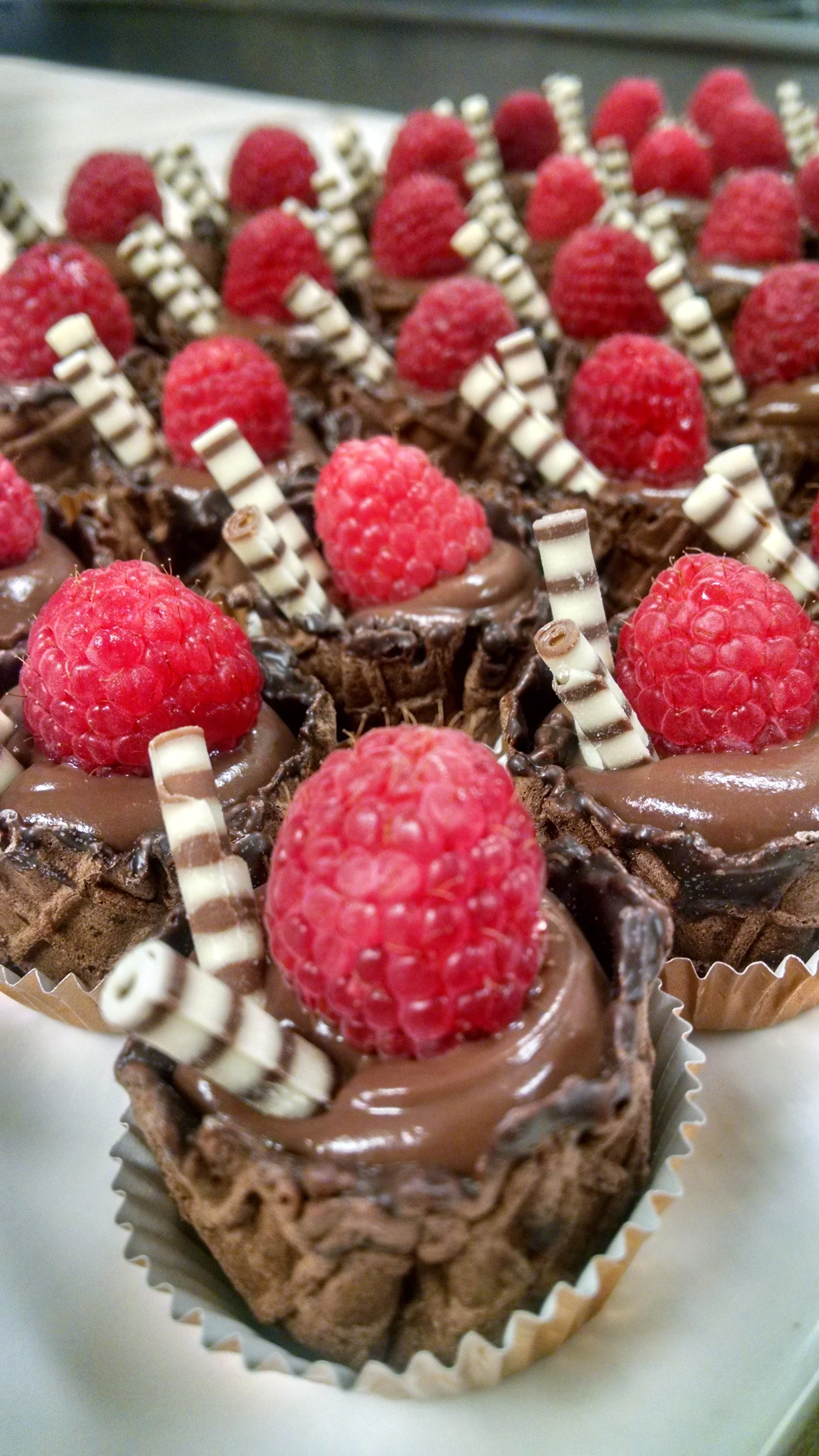 Close-up of individual chocolate tartlets topped with raspberries and white and dark striped chocolate sticks.