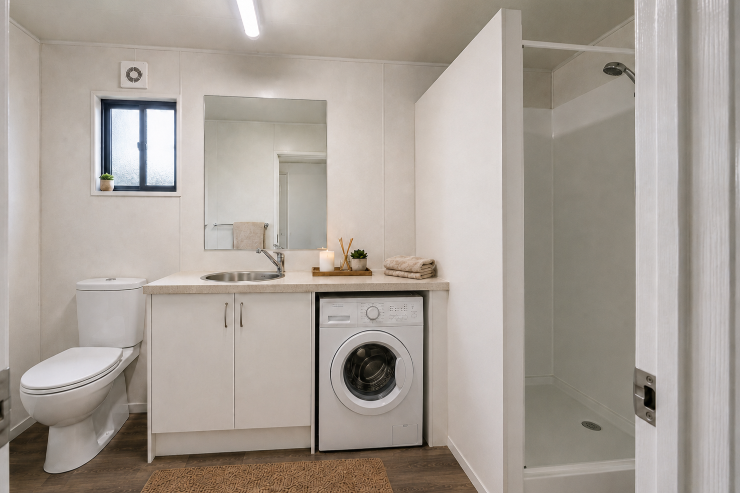 Bathroom with white walls, small window, toilet, mirror, sink, washing machine, candles, towels, and shower area.