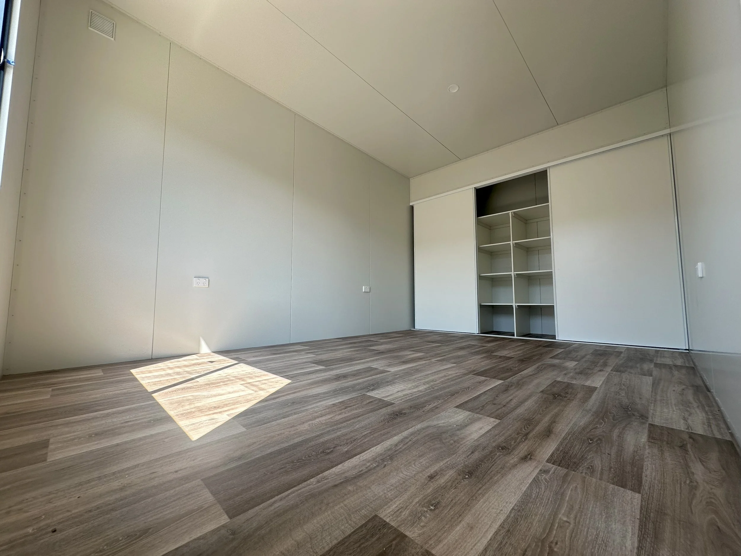 Empty room with wood flooring, white walls, and a built-in open closet with white shelves.