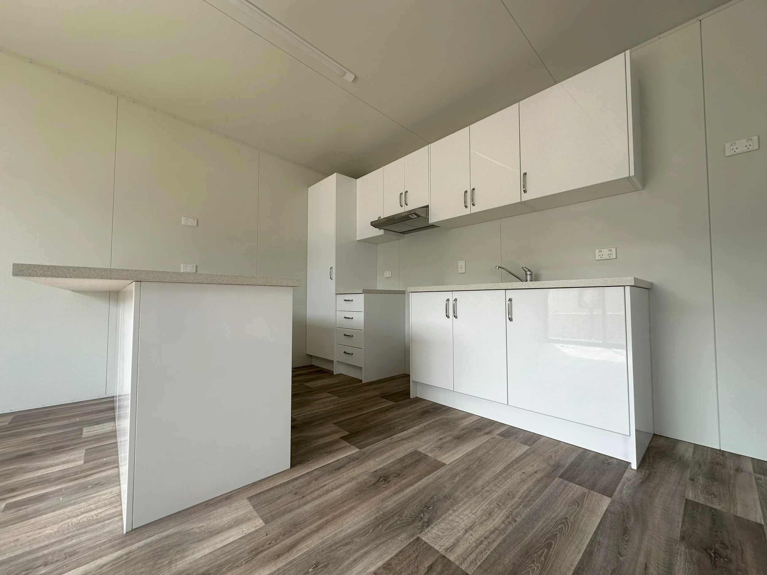 Empty modern kitchen with white cabinets, a countertop, and wood-look flooring.