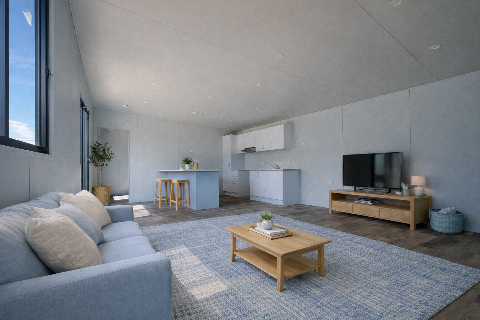 Open-concept living room with a light blue sofa, a wooden coffee table with a potted plant, a large flat-screen TV on a wooden stand, a blue and white area rug, and a kitchen with white cabinets and an island with stools.