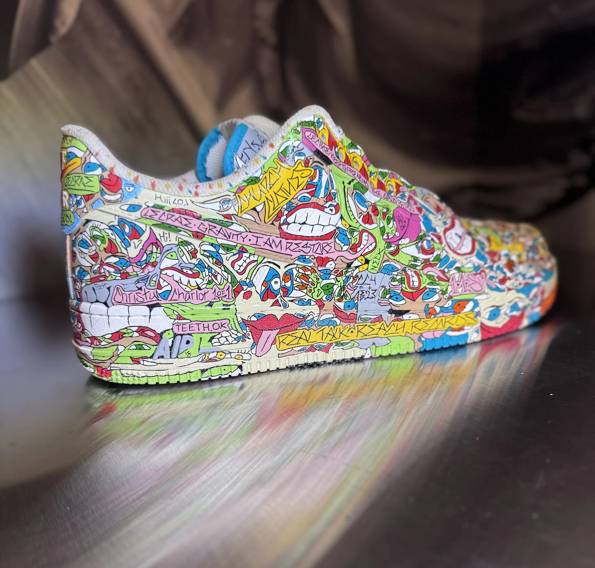 Colorful sneaker with graffiti-style artwork and text, resting on a reflective surface.