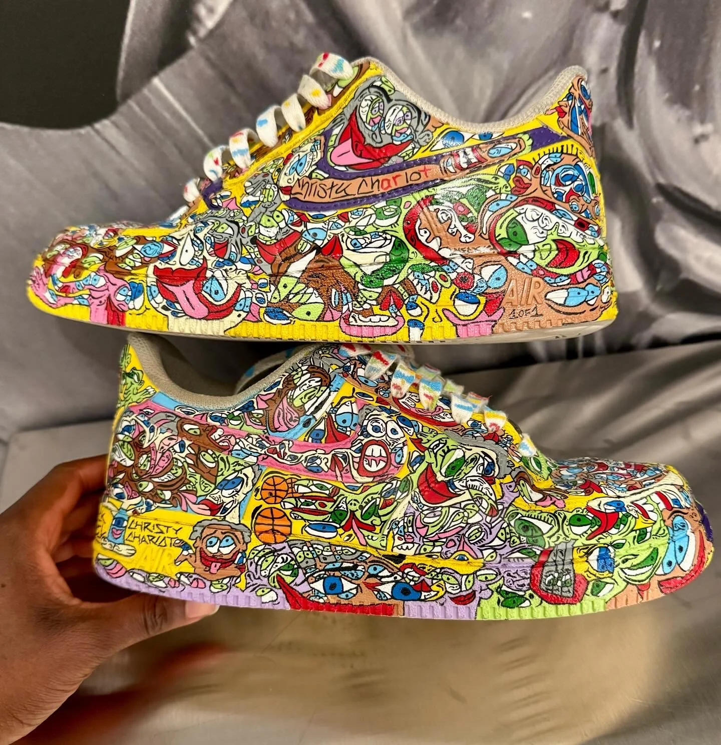 Colorfully decorated sneakers featuring cartoon-style illustrations of characters and faces in vibrant colors, with the words 'Christy Charlotte' on the upper shoe and 'Air' on the sole.