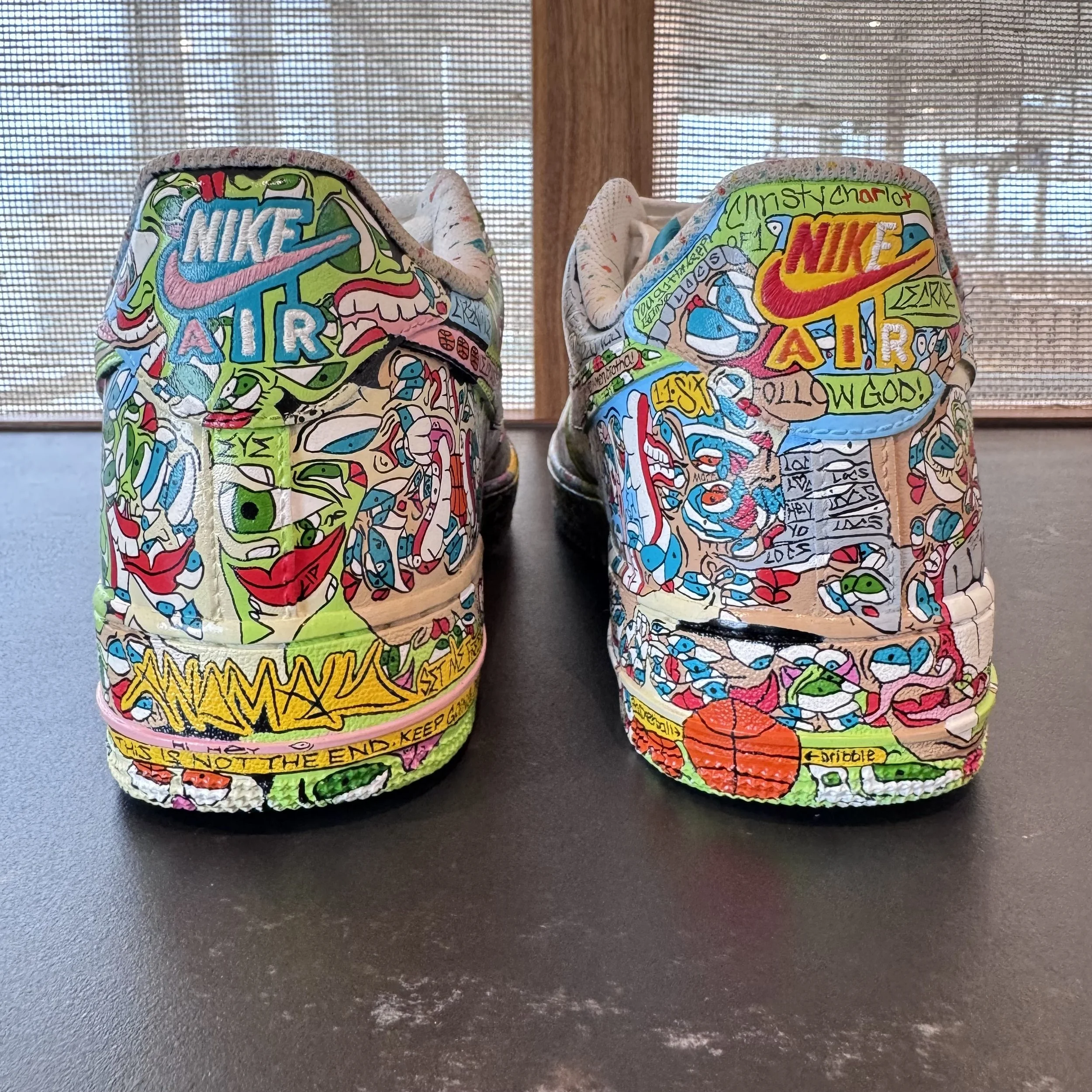 Pair of Nike Air sneakers covered in colorful graffiti-style artwork, featuring various abstract shapes, words, and designs.