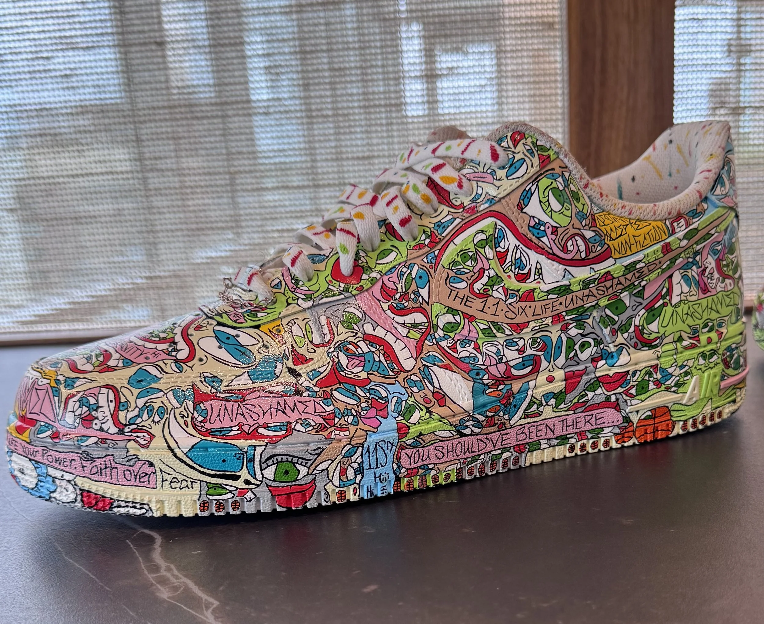 Colorfully painted sneaker with abstract, graffiti-style artwork and text.
