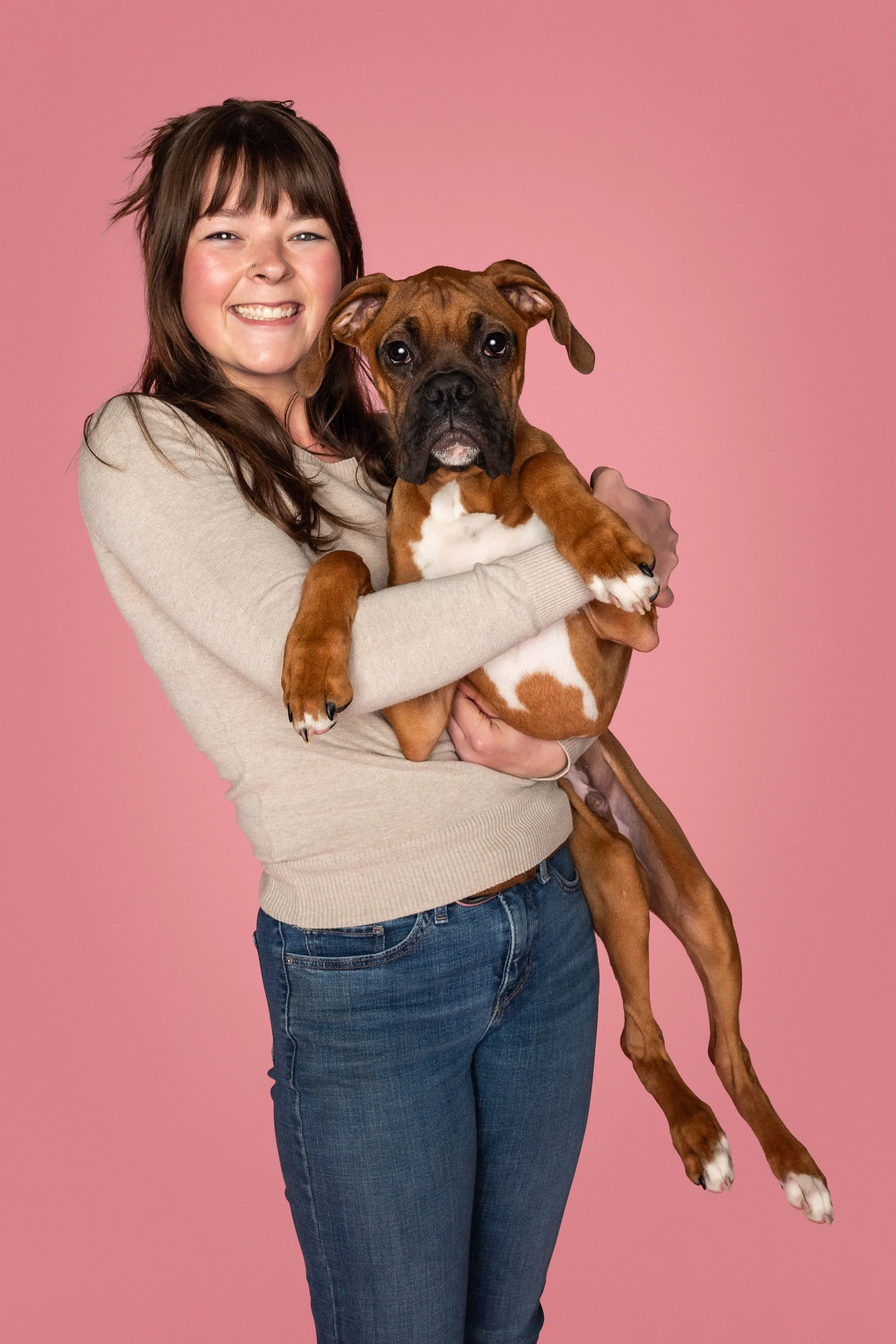 Zoe Heilman holding a boxer puppy in front of a pink studio background.