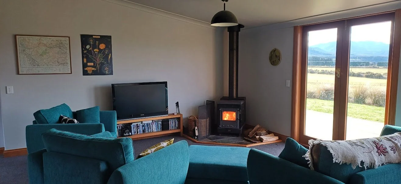 Fantails Rest living room with comfy couches, a wood-burning stove, scenic mountain views, and TV with DVD player.