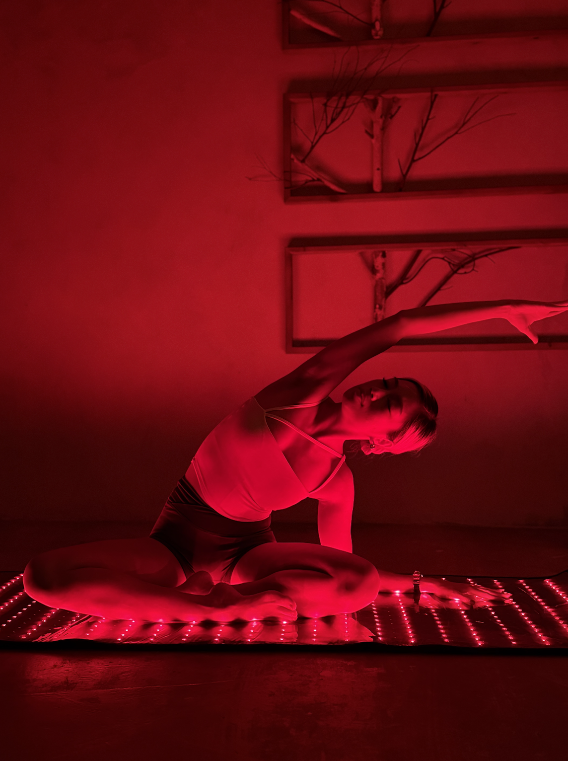 A woman wearing a black athletic tank top and black workout pants, holding her foot behind her while balancing on one leg.