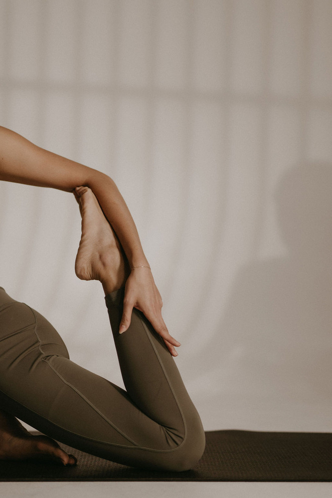 A woman wearing a black athletic tank top and black workout pants, holding her foot behind her while balancing on one leg.