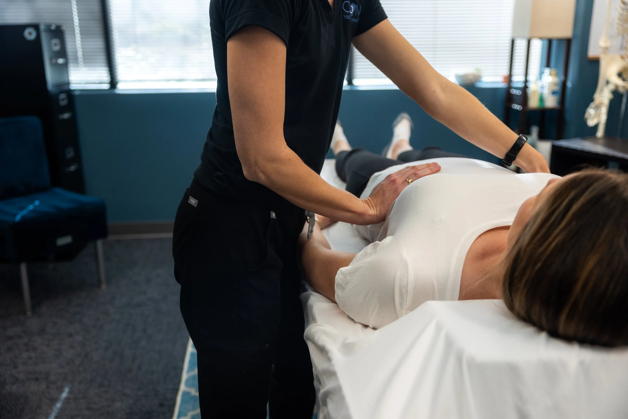 Person performing a physical assessment on a patient lying on an examination table in a clinical setting.